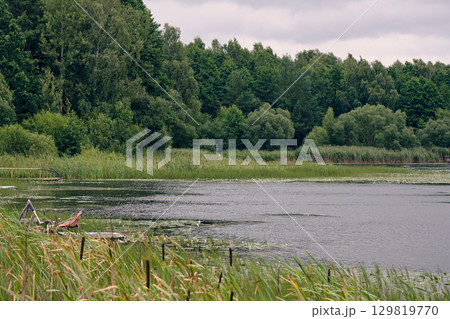 Serene lake surrounded by lush greenery under a cloudy sky in late afternoon 129819770