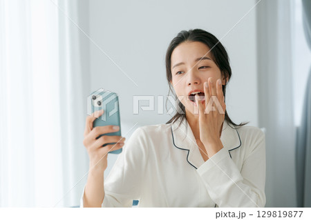 スマホを持つ眠そうな女性 129819877