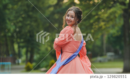 Graduate student wearing academic sash, beaming with pride, spinning joyfully amid green park landscape, symbolizing academic success Graduate student wearing academic sash, beaming with pride, spinning joyfully amid green park landscape, symbolizing academic success 129820551
