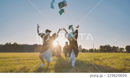 College graduates run into the sunset and throw books and notebooks up in the air. 129820609