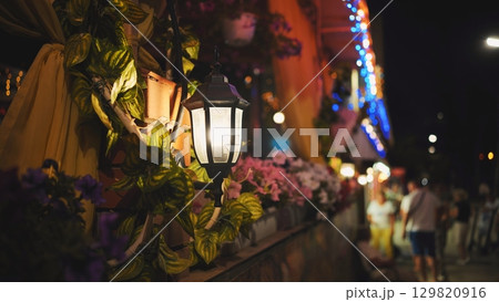 Luminous street lamp adorns a vibrant, flowered facade of a building in crimea, black sea, creating a warm and inviting atmosphere at night 129820916