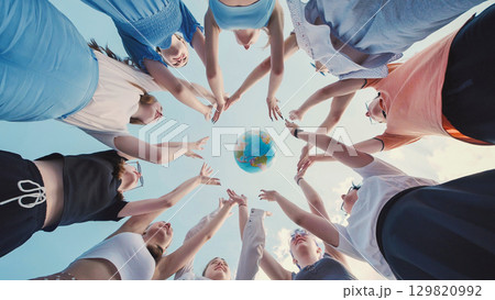 School friends reaching for a globe against a blue sky, representing global unity, environmental awareness, and international collaboration 129820992