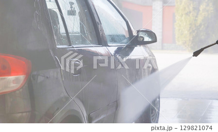 Car wash worker cleaning vehicle with high pressure water jet 129821074