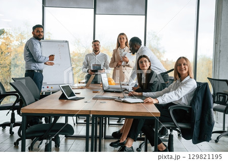 By the table and with whiteboard. Group of office workers are together indoors 129821195