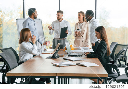 On the meeting, discussing the plans. Group of office workers are together indoors 129821205