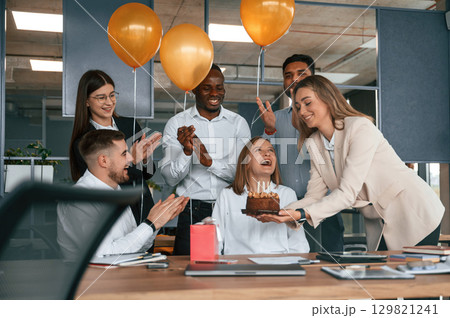 Happy woman is with red gift box. Employee having a birthday in the office, group of workers 129821241