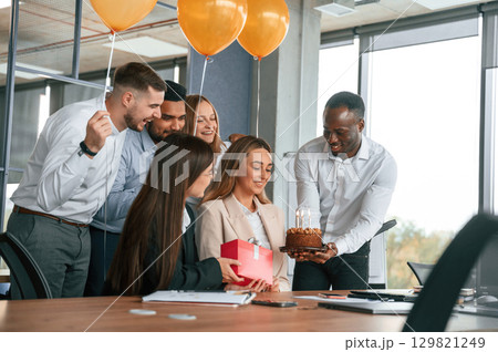 Happy woman is with red gift box. Employee having a birthday in the office, group of workers 129821249