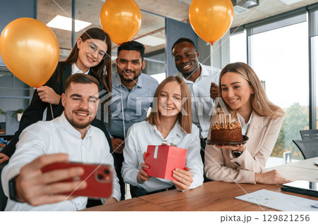 Making selfie with red colored smartphone, with cake. Employee having a birthday in the office, group of workers Making selfie with red colored smartphone, with cake. Employee having a birthday in the office, group of workers 129821256