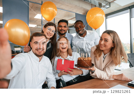 Selfie of happy woman with gift. Employee having a birthday in the office, group of workers 129821261