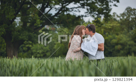 Loving parents sharing gentle kiss, cuddling newborn amid verdant field, capturing intimate family moment of pure connection and happiness Loving parents sharing gentle kiss, cuddling newborn amid verdant field, capturing intimate family moment of pure connection and happiness 129821394
