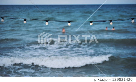 String of lights illuminating the beach of Crimea with tourists swimming in the sea 129821420