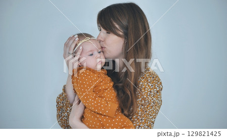 Young mother kissing her baby girl on the forehead, showing love and care in a heartwarming family moment Young mother kissing her baby girl on the forehead, showing love and care in a heartwarming family moment 129821425