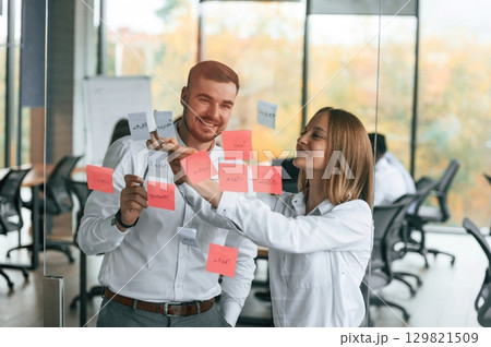 Two people are putting stickers on the glass. Planning the project. Group of office workers are together indoors 129821509