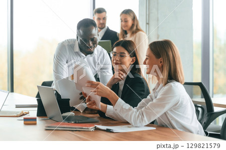 Wireless device on the table, laptop. Group of office workers are together indoors 129821579