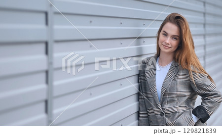 Confident businesswoman wearing checkered blazer, leaning against corrugated metal wall, radiating professional elegance Confident businesswoman wearing checkered blazer, leaning against corrugated metal wall, radiating professional elegance 129821839