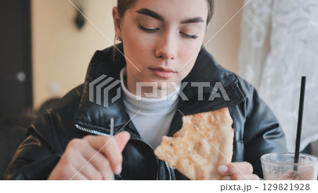 Young woman biting pizza slice, smiling while dining casually with friends Young woman biting pizza slice, smiling while dining casually with friends 129821928