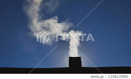 White smoke rising from chimney, contrasting sharply with vibrant blue sky and sunlight streaming across winter landscape White smoke rising from chimney, contrasting sharply with vibrant blue sky and sunlight streaming across winter landscape 129822066