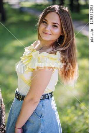 Teenage girl smiling, standing in park, wearing yellow top and denim skirt Teenage girl smiling, standing in park, wearing yellow top and denim skirt 129822098