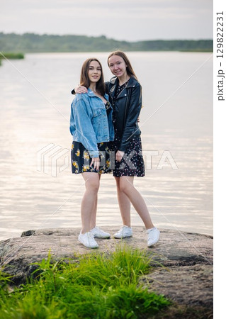 Two young women hugging each other, standing on a rock by the lake, enjoying their friendship Two young women hugging each other, standing on a rock by the lake, enjoying their friendship 129822231