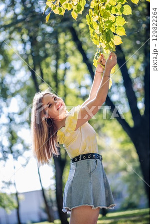 Teenager girl enjoying a sunny autumn day in a park, reaching for golden leaves on a tree branch Teenager girl enjoying a sunny autumn day in a park, reaching for golden leaves on a tree branch 129822264