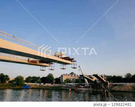 Construction workers raising prefabricated bridge segments using large cranes near Vistula River in Krakow, Poland, highlighting urban infrastructure progress and engineering complexity. Construction Construction workers raising prefabricated bridge segments using large cranes near Vistula River in Krakow, Poland, highlighting urban infrastructure progress and engineering complexity. Construction 129822481