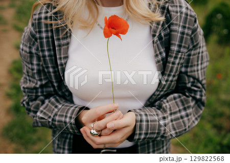 Close up of young blonde woman gently cradling vibrant red poppy flower, embodying themes of remembrance, peace, and beauty found in nature delicate wonders. Woman delicately holding vibrant red poppy Close up of young blonde woman gently cradling vibrant red poppy flower, embodying themes of remembrance, peace, and beauty found in nature delicate wonders. Woman delicately holding vibrant red poppy 129822568