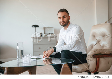 Elegant man in formal clothes is sitting indoors at his cabinet Elegant man in formal clothes is sitting indoors at his cabinet 129822903