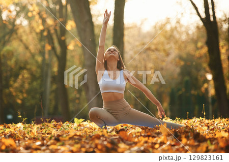 Conception of flexibility. Young beautiful woman is doing yoga in the autumn park Conception of flexibility. Young beautiful woman is doing yoga in the autumn park 129823161