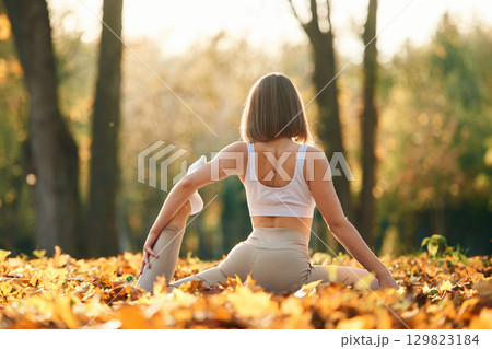 Legs flexibility. Young beautiful woman is doing yoga in the autumn park Legs flexibility. Young beautiful woman is doing yoga in the autumn park 129823184
