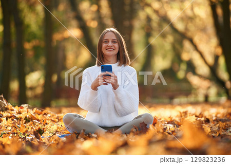 Woman is sitting in the autumn park or forest with smartphone in hands 129823236