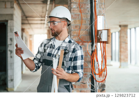 Planning the project, with paper. Construction worker in uniform in empty unfinished room 129823712