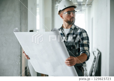 Project on the paper, holding in hands. Construction worker in uniform in empty unfinished room Project on the paper, holding in hands. Construction worker in uniform in empty unfinished room 129823723