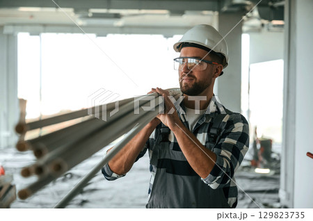 Plastic tubes in hands. Construction worker in uniform in empty unfinished room Plastic tubes in hands. Construction worker in uniform in empty unfinished room 129823735