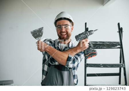 With drill. Repairman in uniform is in the unfinished building With drill. Repairman in uniform is in the unfinished building 129823743