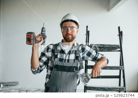 With drill. Repairman in uniform is in the unfinished building 129823744