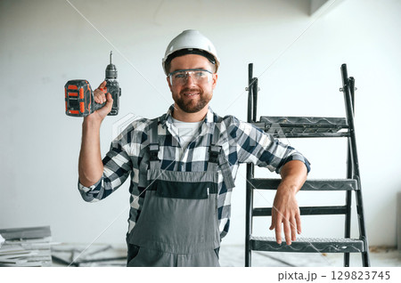 With drill. Repairman in uniform is in the unfinished building With drill. Repairman in uniform is in the unfinished building 129823745
