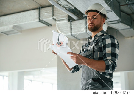 Checking the ceiling. Construction worker in uniform in empty unfinished room Checking the ceiling. Construction worker in uniform in empty unfinished room 129823755