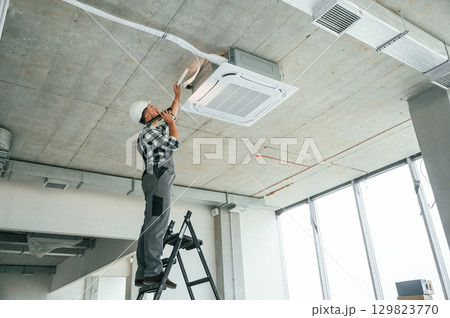 Fixing ventilation system. Repairman in uniform is in the unfinished building 129823770