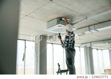 Fixing ventilation system. Repairman in uniform is in the unfinished building Fixing ventilation system. Repairman in uniform is in the unfinished building 129823771