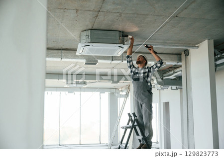 Setting the ventilation system. Repairman in uniform is in the unfinished building 129823773