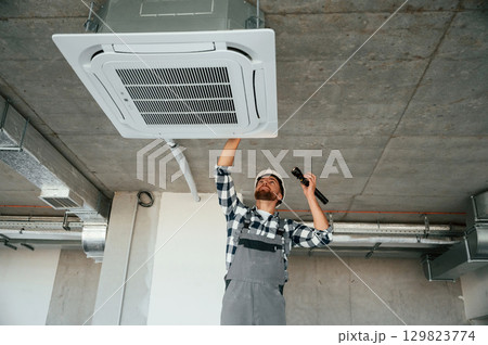 Using flashlight. Repairman in uniform is in the unfinished building 129823774