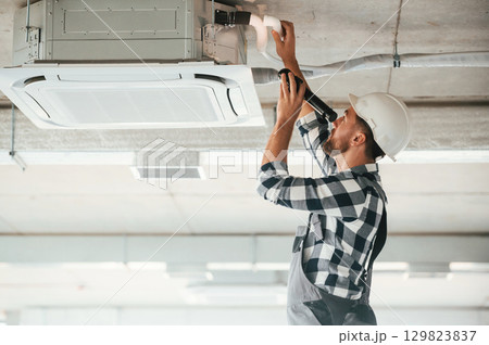 Setting up the ventilation system on the ceiling. Repairman in uniform is in the unfinished building Setting up the ventilation system on the ceiling. Repairman in uniform is in the unfinished building 129823837