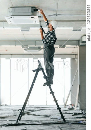 Standing on the ladder. Repairman in uniform is in the unfinished building 129823843