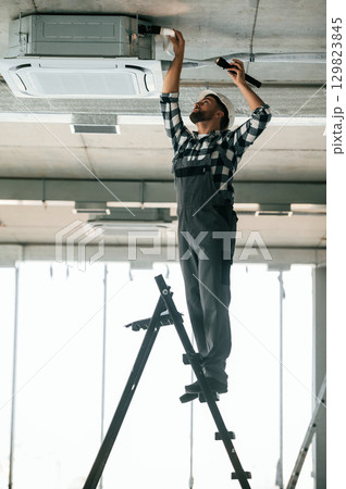 Standing on the ladder. Repairman in uniform is in the unfinished building 129823845