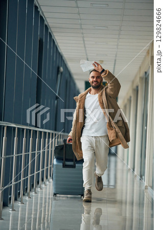 Running, late for flight, with tickets in hand. Young handsome man in the airport Running, late for flight, with tickets in hand. Young handsome man in the airport 129824666