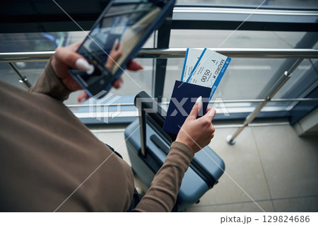 Holding smartphone. Close up view of female traveler in airport hall with tickets Holding smartphone. Close up view of female traveler in airport hall with tickets 129824686