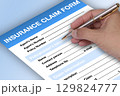 Someone hand holding a pen to fill out an insurance claim form. 129824777