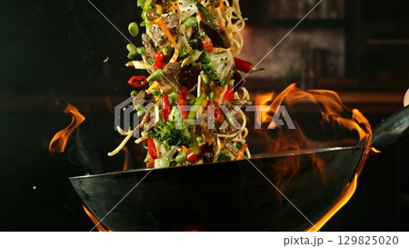 Freeze Motion of Wok Pan with Flying Ingredients in the Air and Fire Flames. Kitchen Interior on Background. Freeze Motion of Wok Pan with Flying Ingredients in the Air and Fire Flames. Kitchen Interior on Background. 129825020
