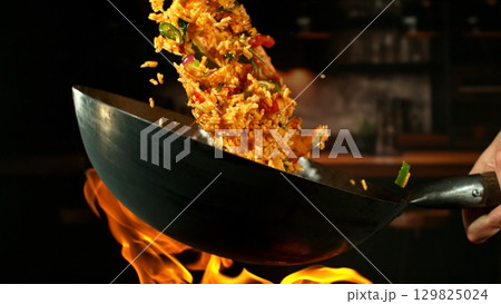 Freeze Motion of Wok Pan with Flying Spanish Paella up in the Air and Fire Flames. Kitchen Interior on Background. 129825024