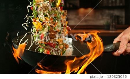 Freeze Motion of Wok Pan with Flying Ingredients in the Air and Fire Flames. Kitchen Interior on Background. 129825026